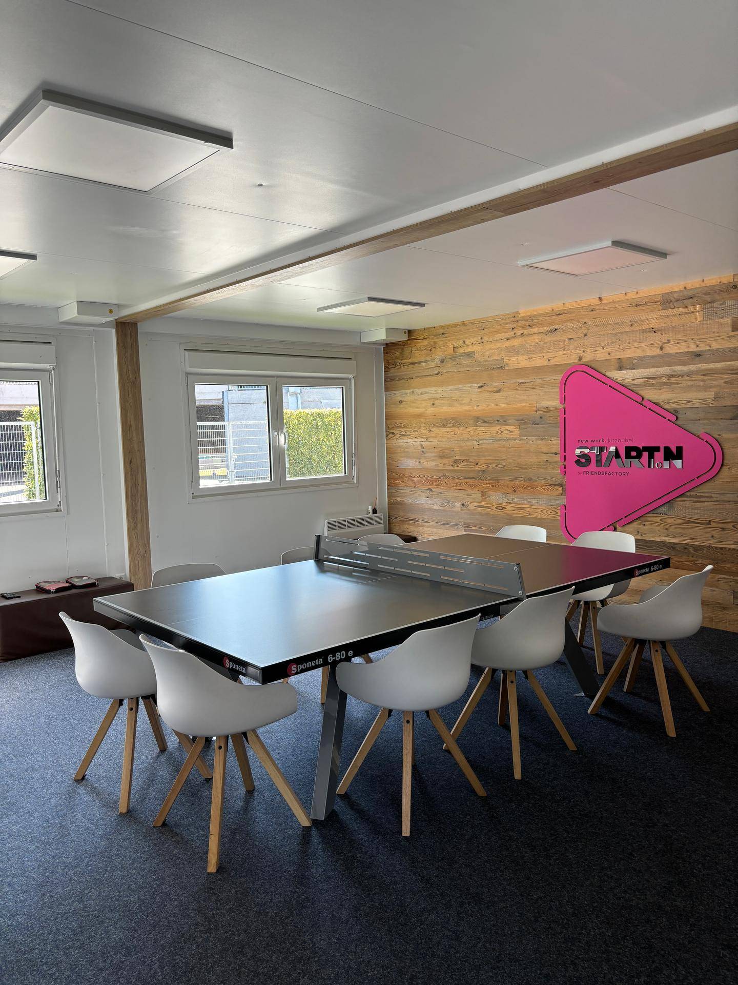 Vielseitiger Gemeinschaftsraum mit Tischtennisplatte, modernen Stühlen und einer dekorativen Holzwand.