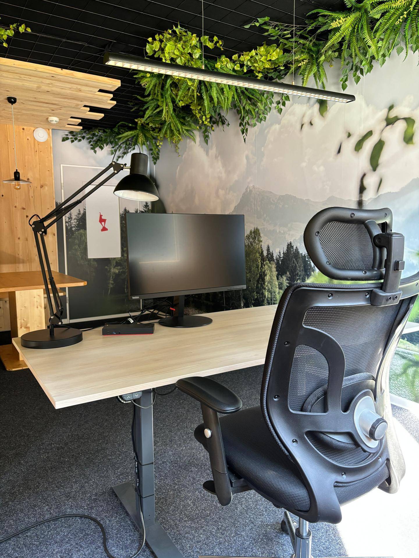 Moderner Arbeitsplatz mit ergonomischem Stuhl, höhenverstellbarem Schreibtisch und kreativer Wandgestaltung.