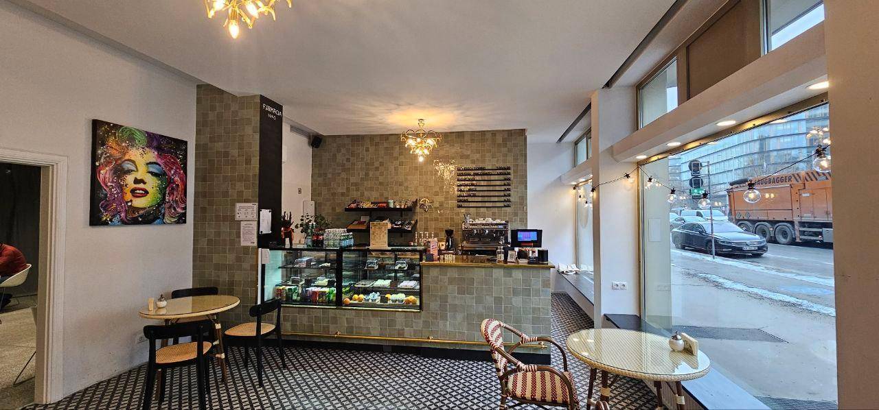 Gesamtansicht des Cafés mit Theke, Kuchenvitrine und Sitzgelegenheiten, beleuchtet von Kronleuchtern.