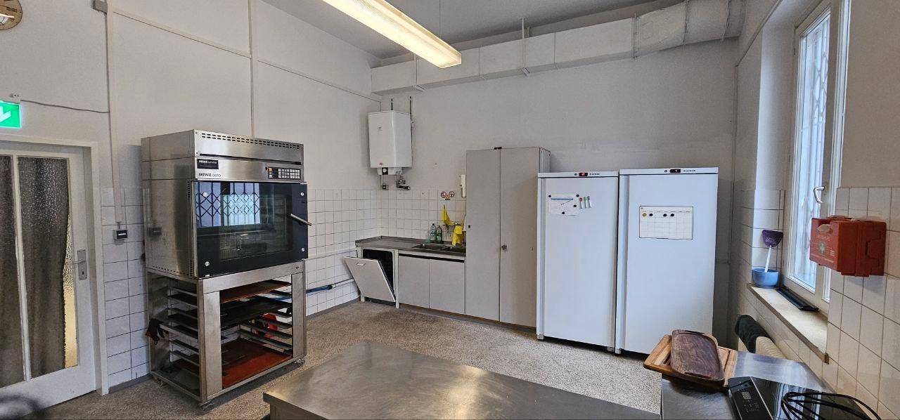 Große Gewerbeküche mit professionellem Ofen, zwei Kühlschränken und gefliesten Wänden.