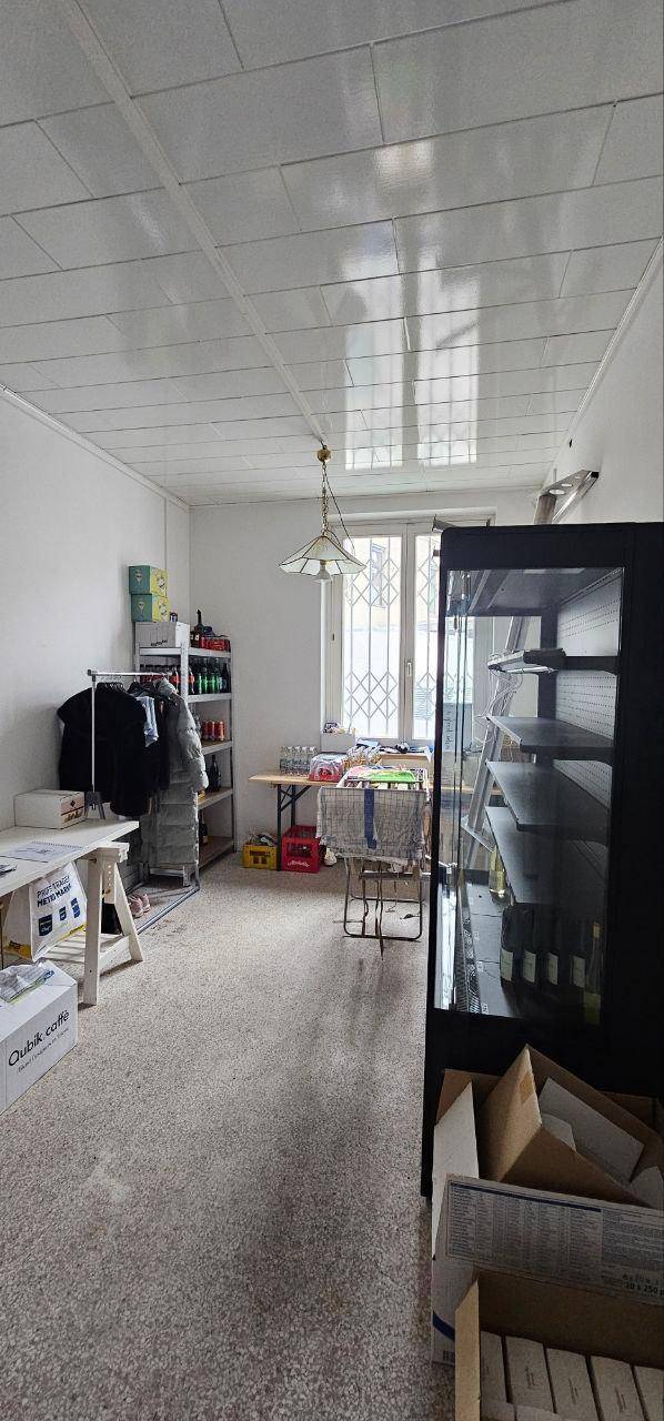 Lagerraum oder Hinterzimmer mit Regalen, Kartons und einem Fenster mit Sicherheitsgittern.