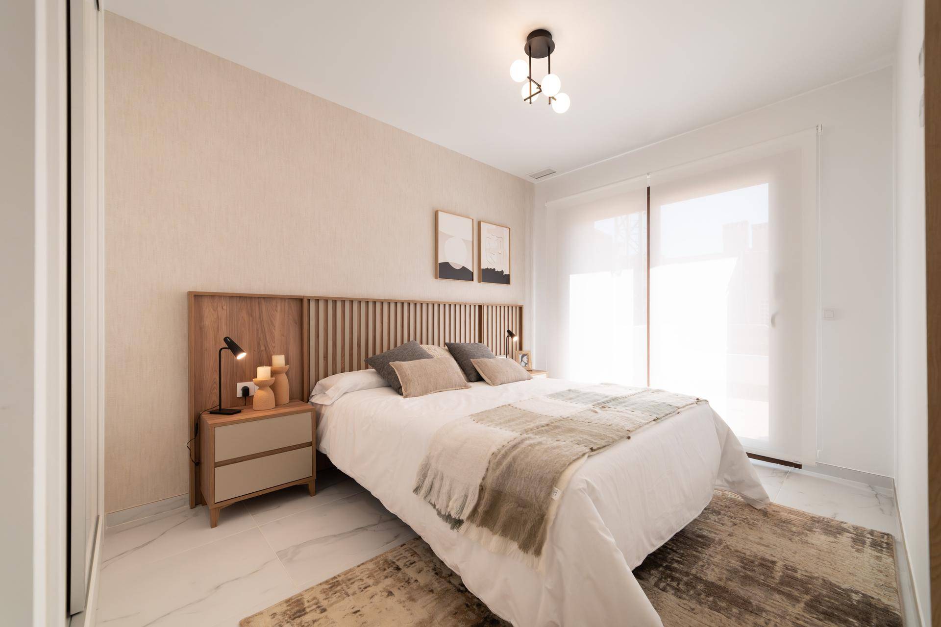 Helles Schlafzimmer mit großem Bett, Holzkopfteil und Zugang zu einem Balkon oder Terrasse.