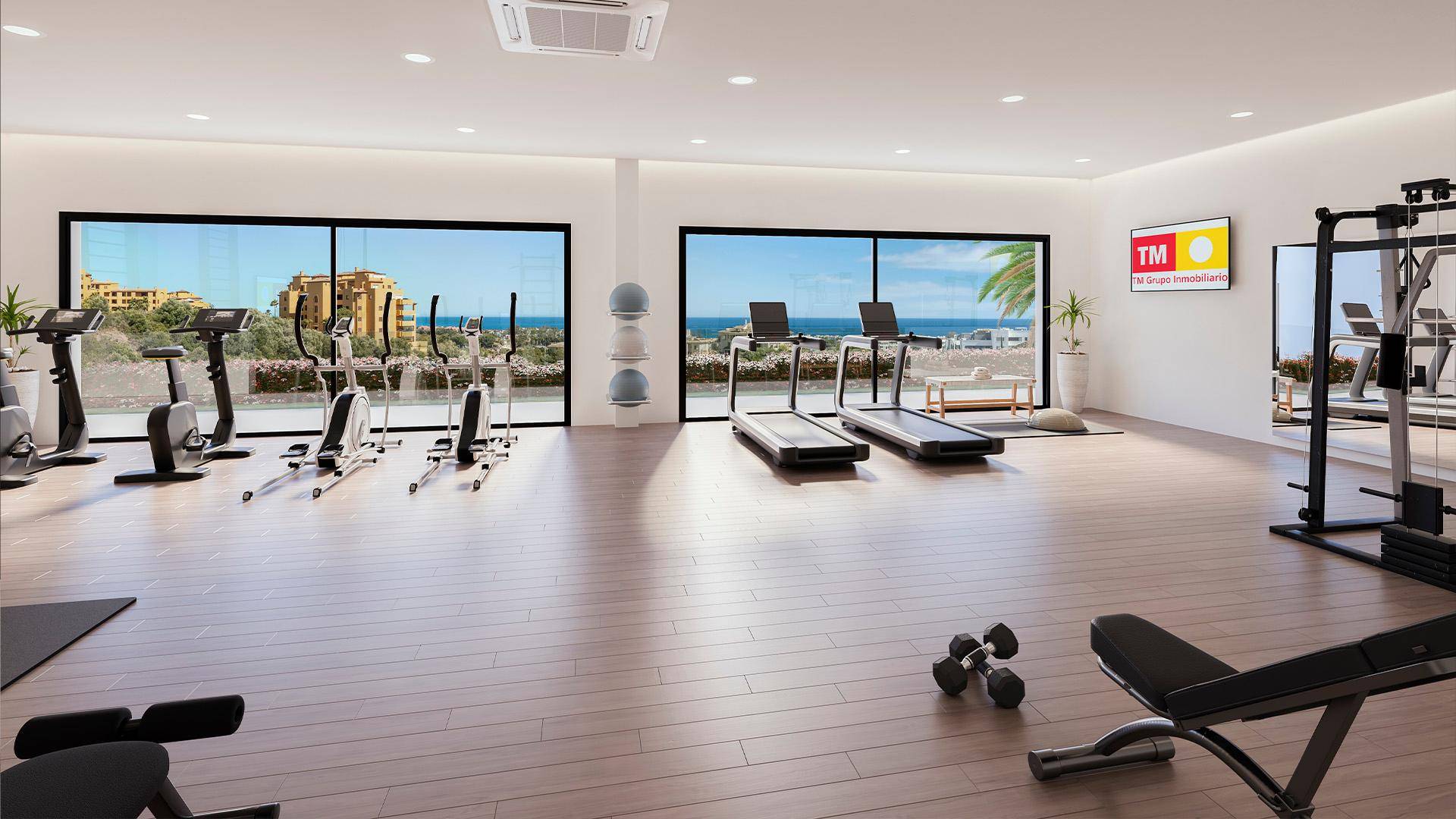 Moderner Fitnessraum mit verschiedenen Geräten, großen Fenstern und Meerblick.