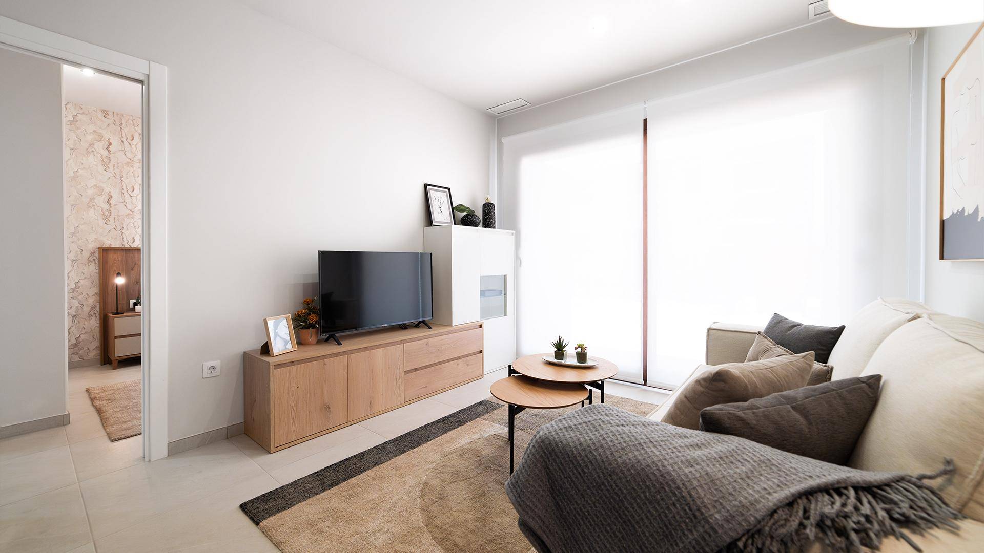 Helles Wohnzimmer mit TV-Möbeln aus Holz, beigem Sofa und Zugang zu einem anderen Raum.