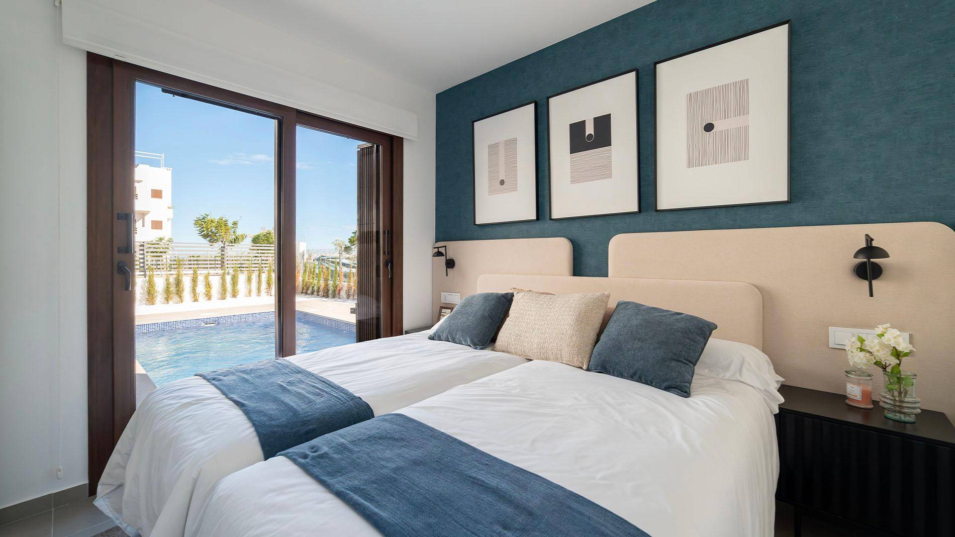 Schlafzimmer mit zwei Einzelbetten, blauer Akzentwand und direktem Zugang zum Poolbereich.