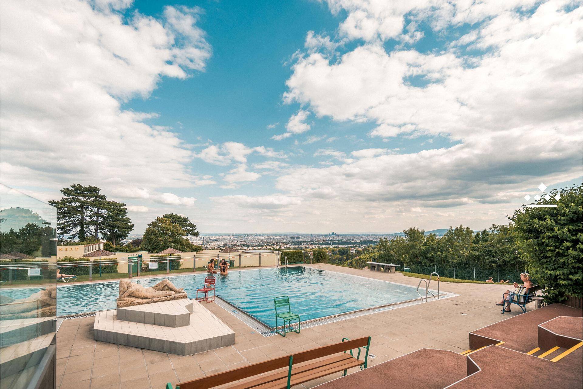 Großzügige Freibadanlage mit mehreren Becken und Panoramablick auf die Stadt unter blauem Himmel.