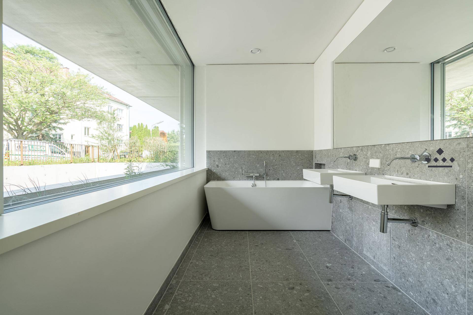 Geräumiges Badezimmer mit großer Badewanne, Doppelwaschbecken und breitem Fenster für Tageslicht.
