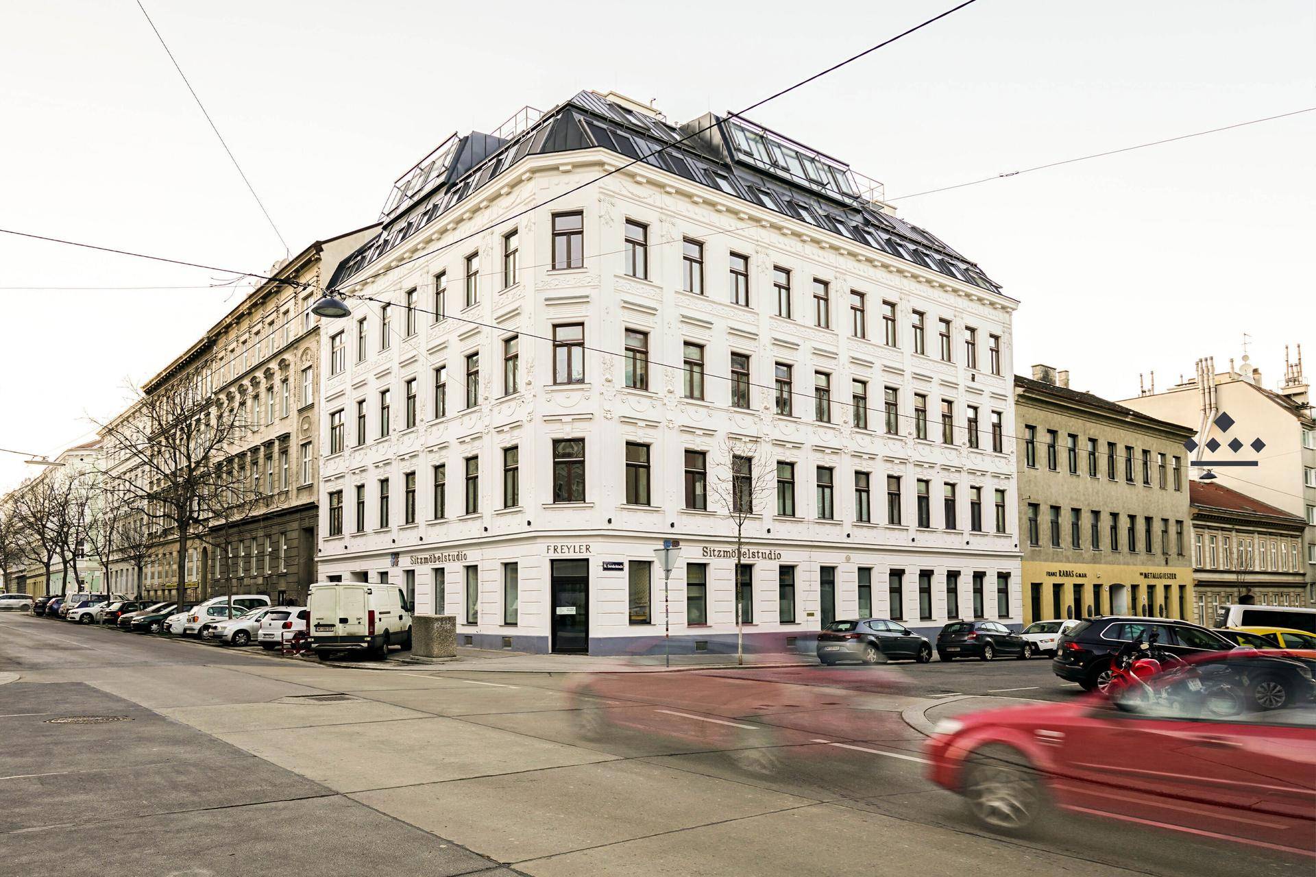Elegantes Eckgebäude mit klassischer Architektur und modernen Dachaufbauten in städtischer Umgebung.