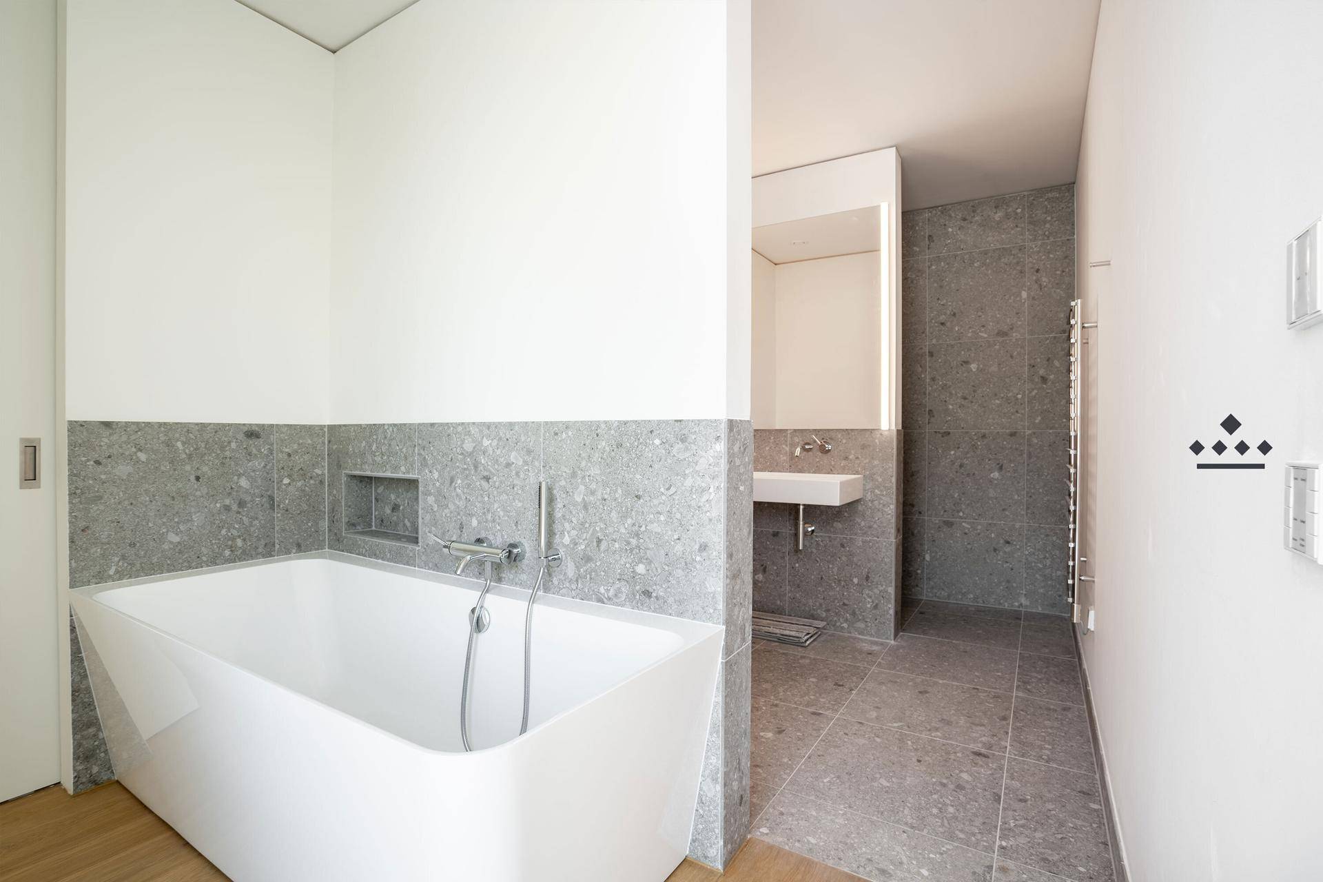 Modernes Badezimmer mit Badewanne, grauen Fliesen und minimalistischem Design.
