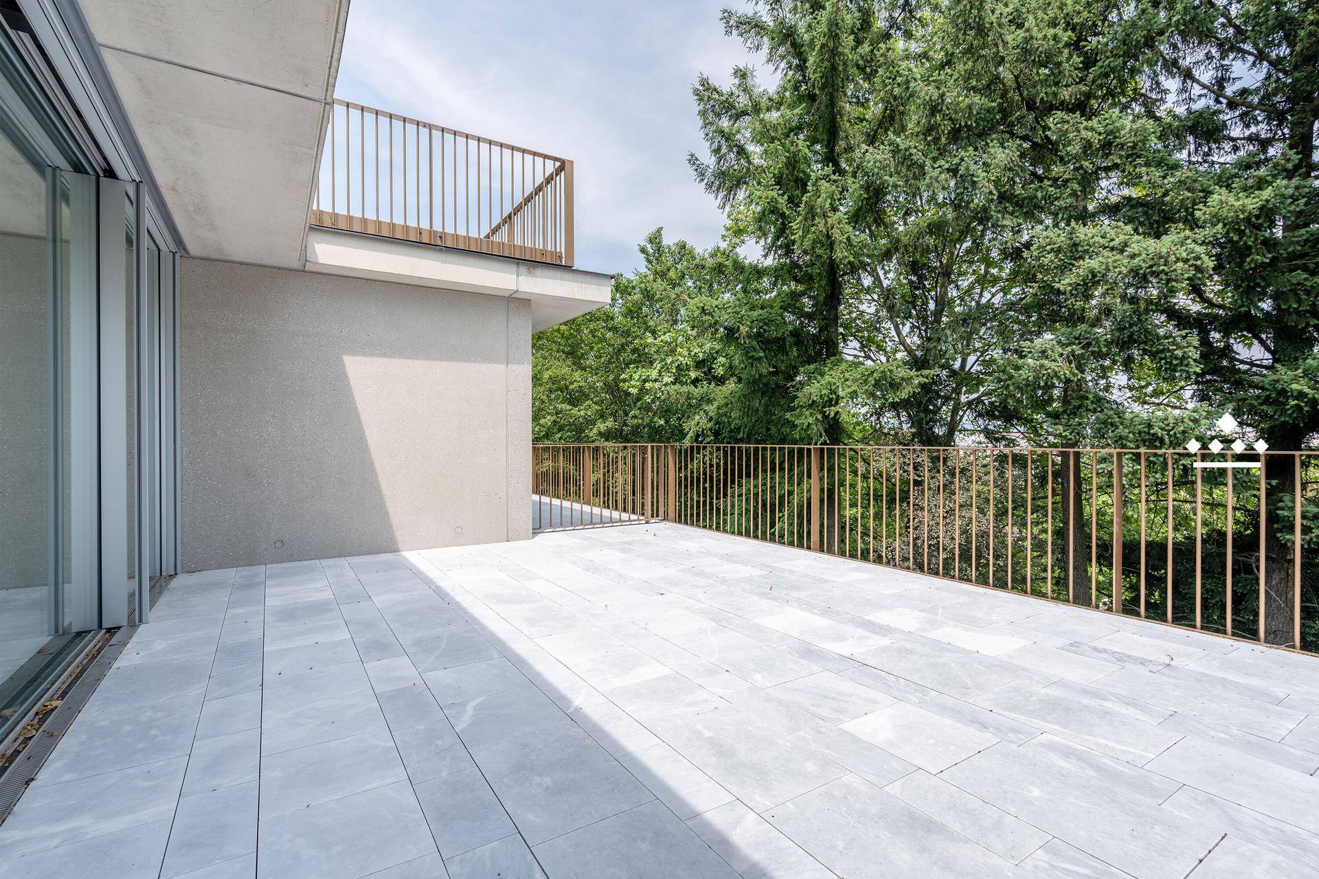Große, geflieste Terrasse mit Metallgeländer und Blick ins Grüne.