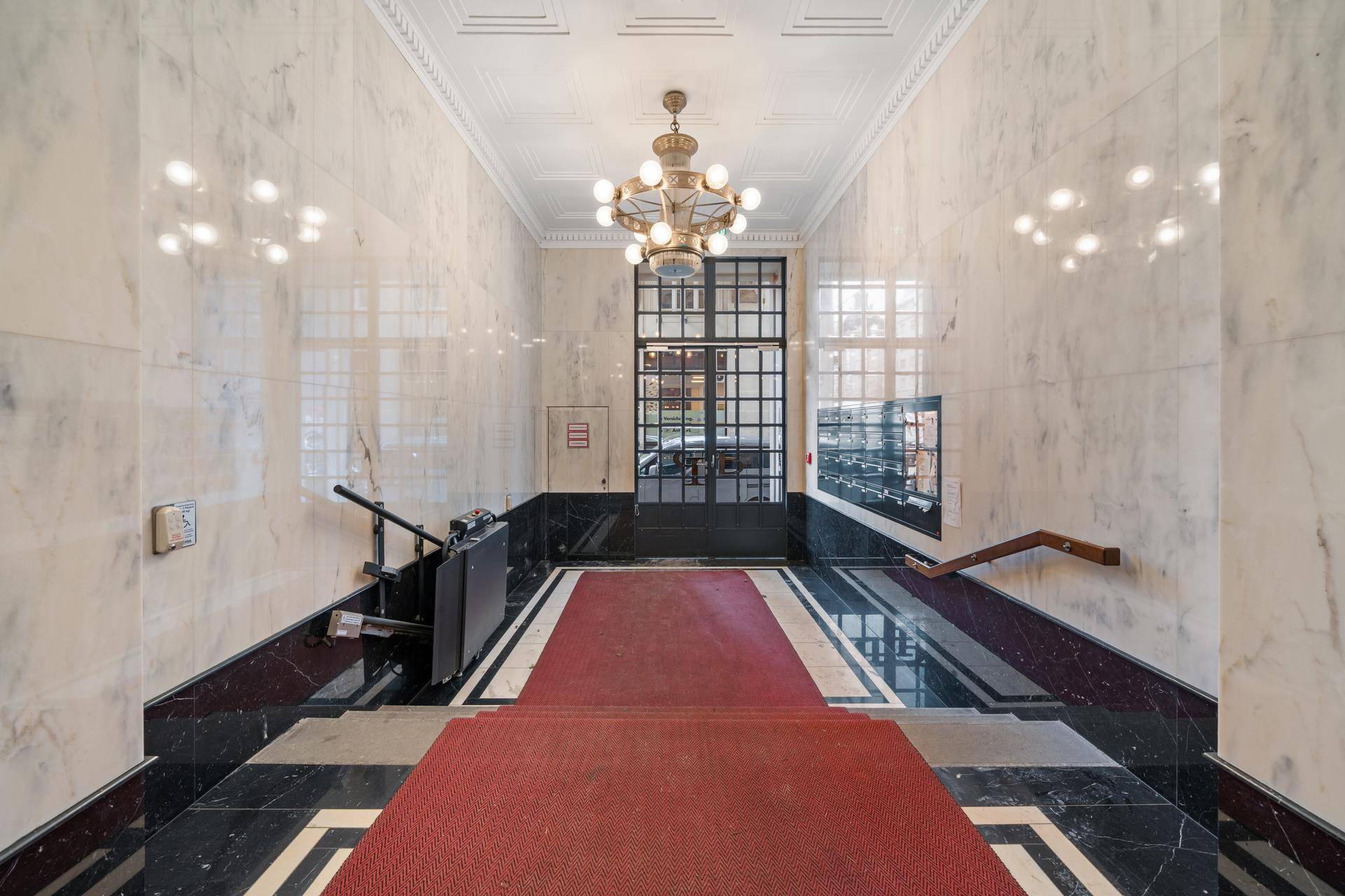 Elegante Eingangshalle mit Marmorverkleidung, rotem Teppich und Zugang zur Treppe.