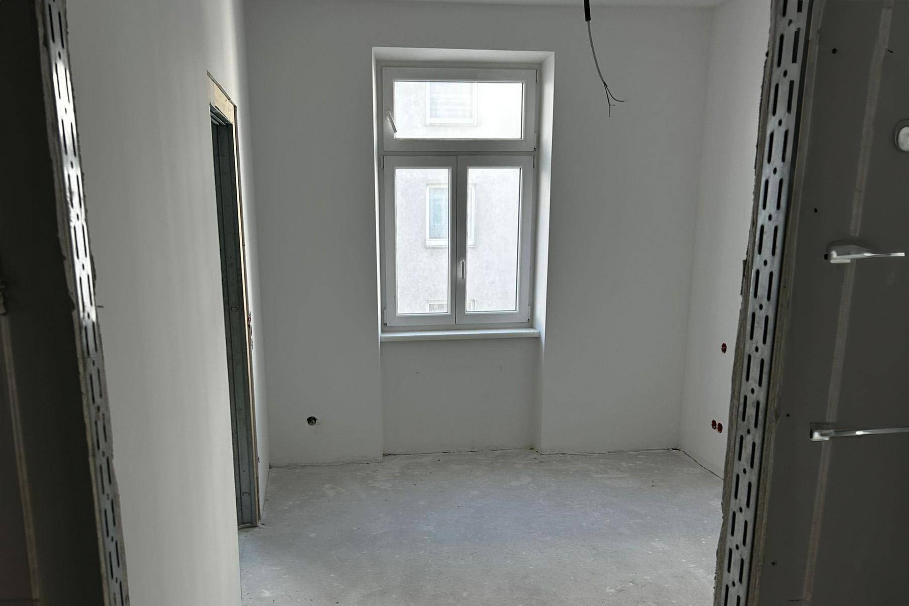 Unfertiger Raum mit einem Fenster und sichtbaren Holzbalken, bereit für die weitere Gestaltung.