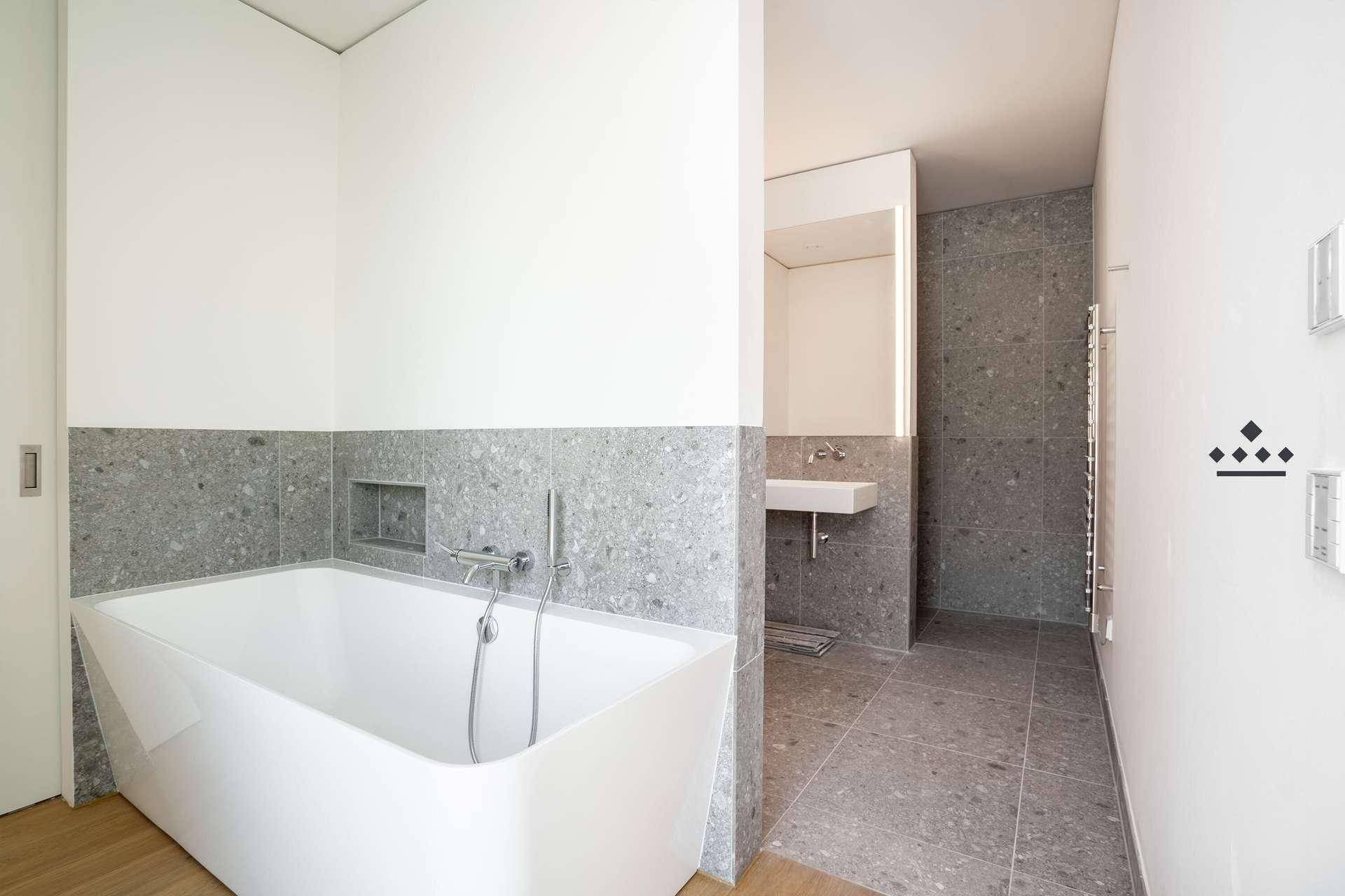 Modernes Badezimmer mit freistehender Badewanne, grauen Fliesen und minimalistischem Design.