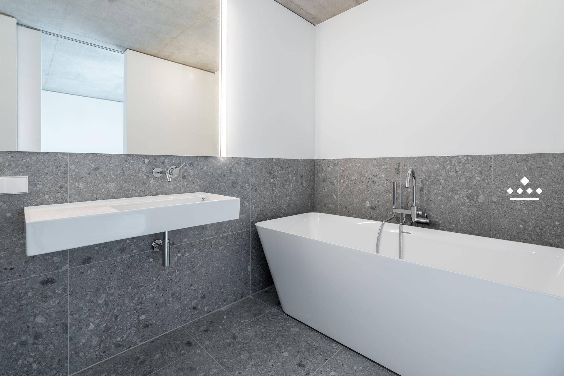 Modernes Badezimmer mit freistehender Badewanne, Wandwaschbecken und grauen Fliesen.