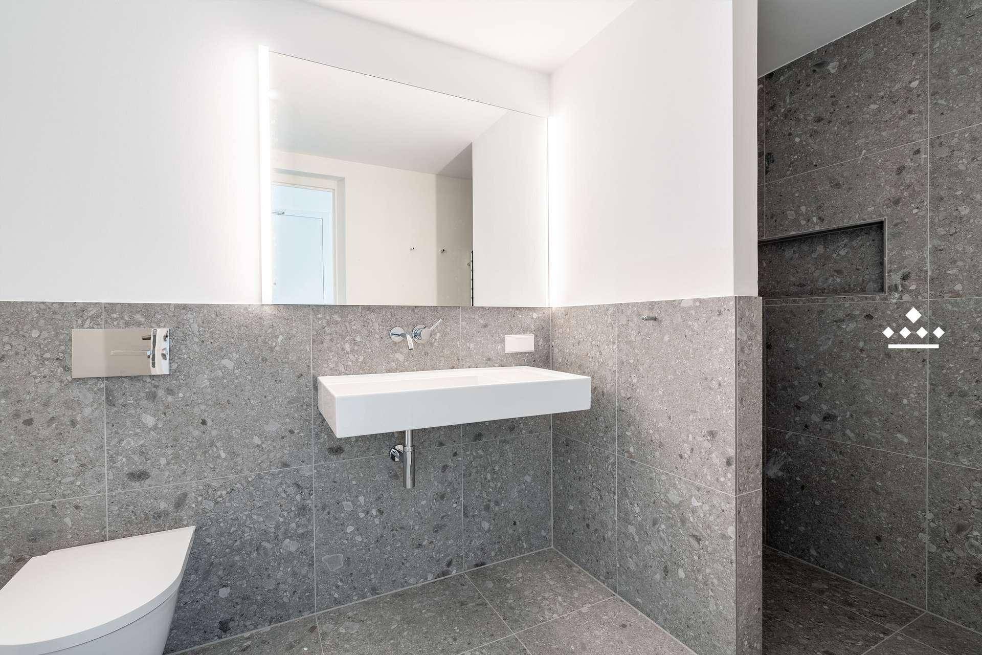 Modernes Badezimmer mit grauen Fliesen, wandhängendem WC und elegantem Waschtisch.