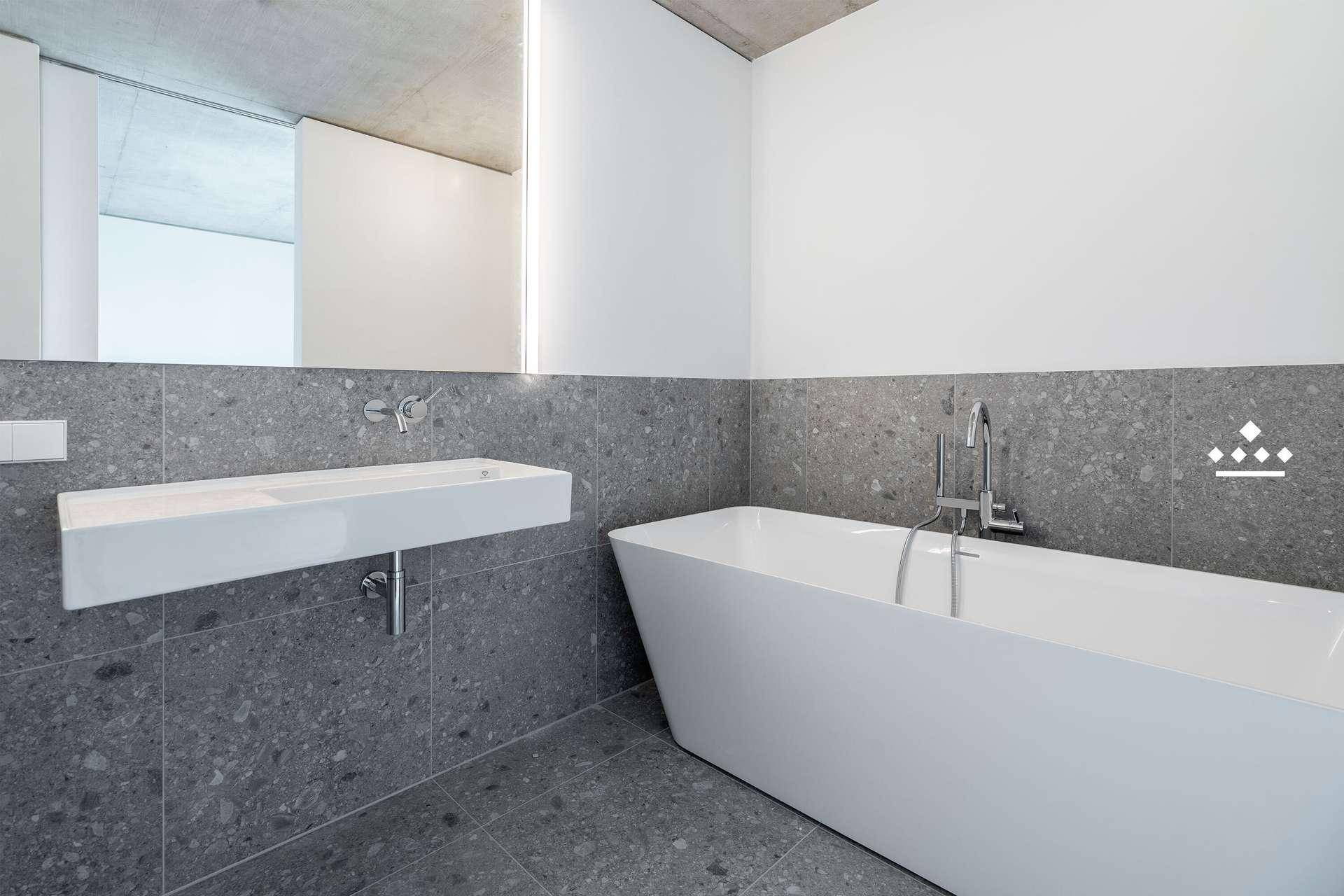 Modernes Badezimmer mit freistehender Badewanne, Wandwaschbecken und grauen Fliesen.