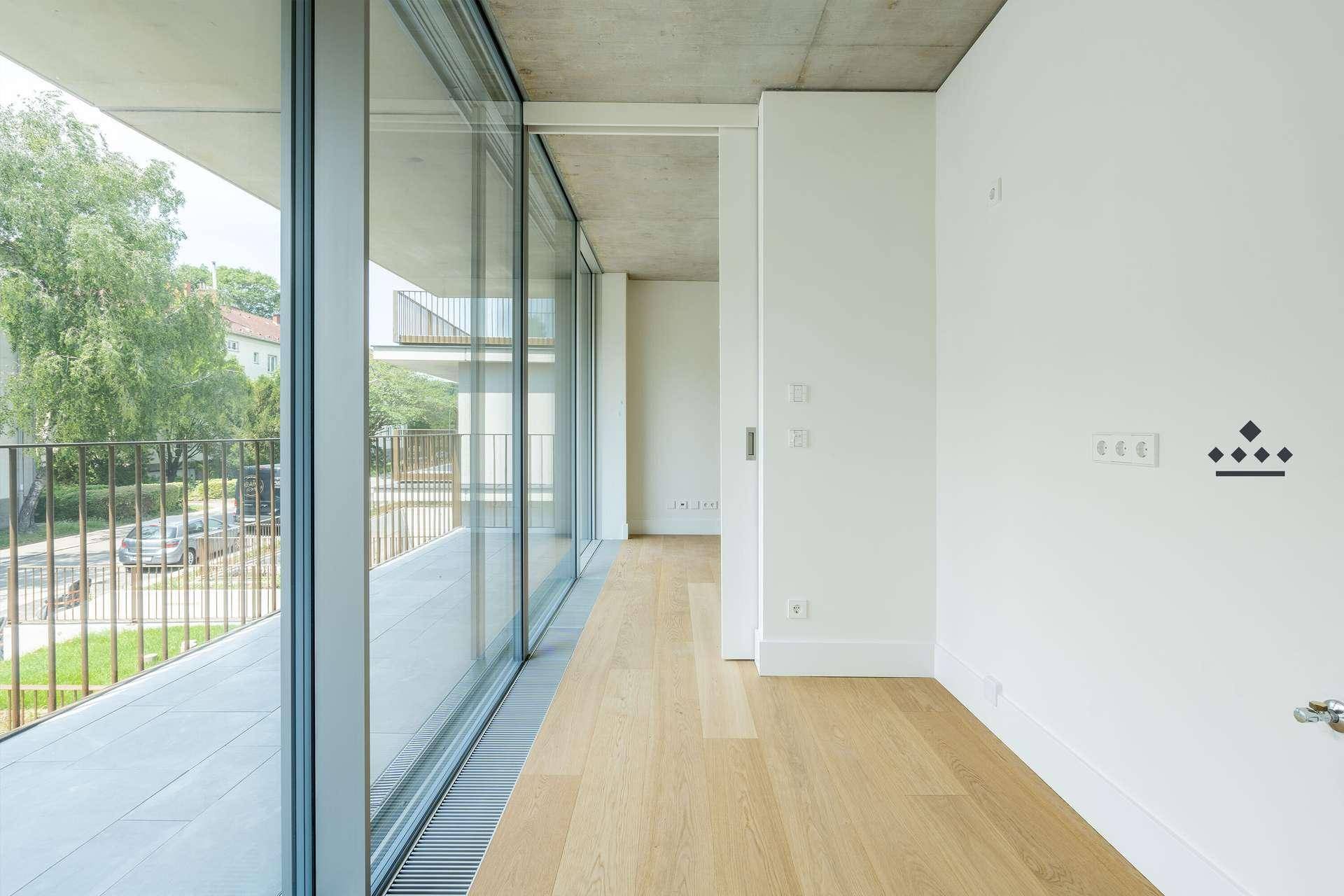 Langer, heller Flur mit Holzboden und raumhohen Schiebetüren, die zu einem Balkon führen.
