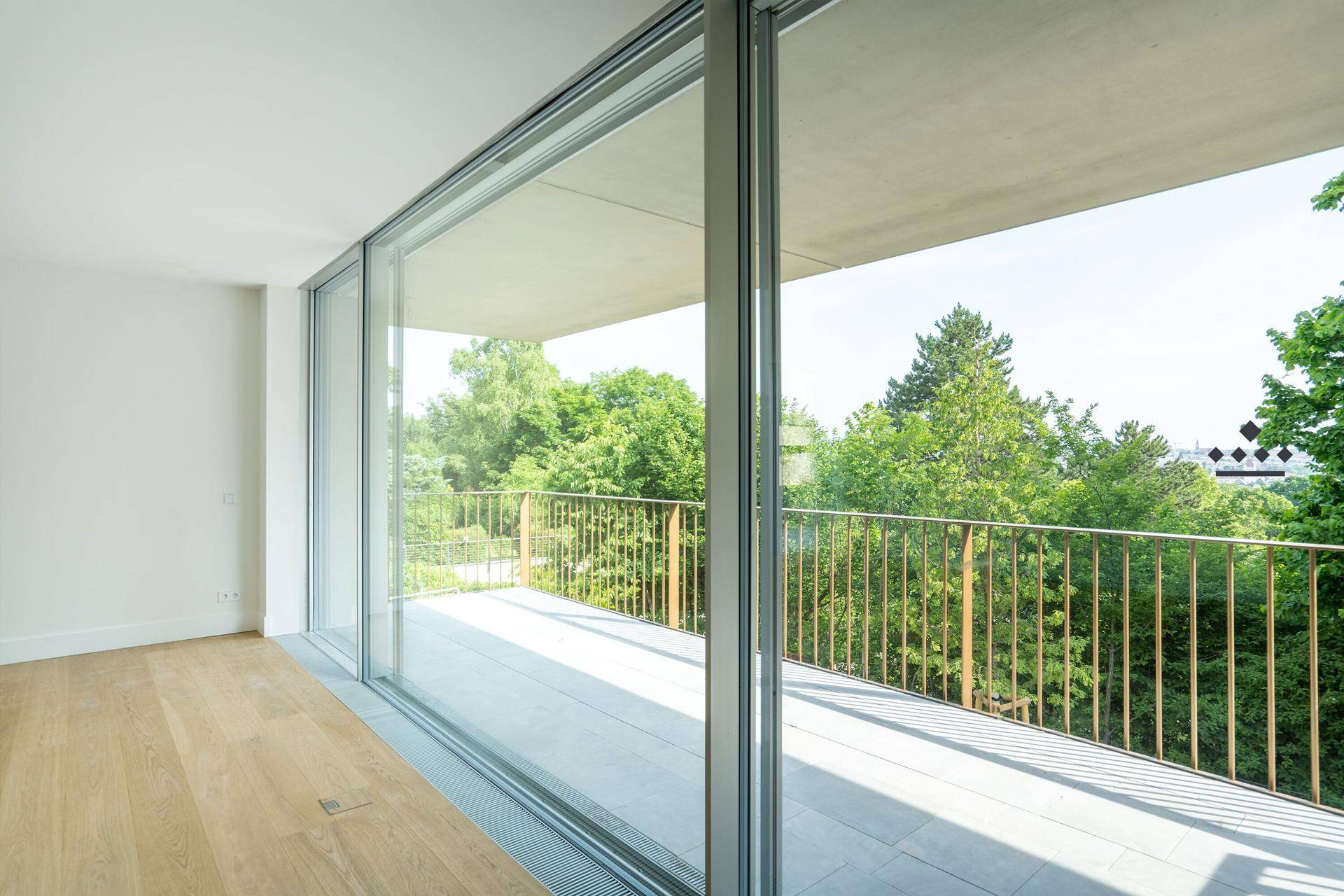 Heller Raum mit Parkettboden und raumhohen Schiebetüren, die zu einem großen Balkon führen.