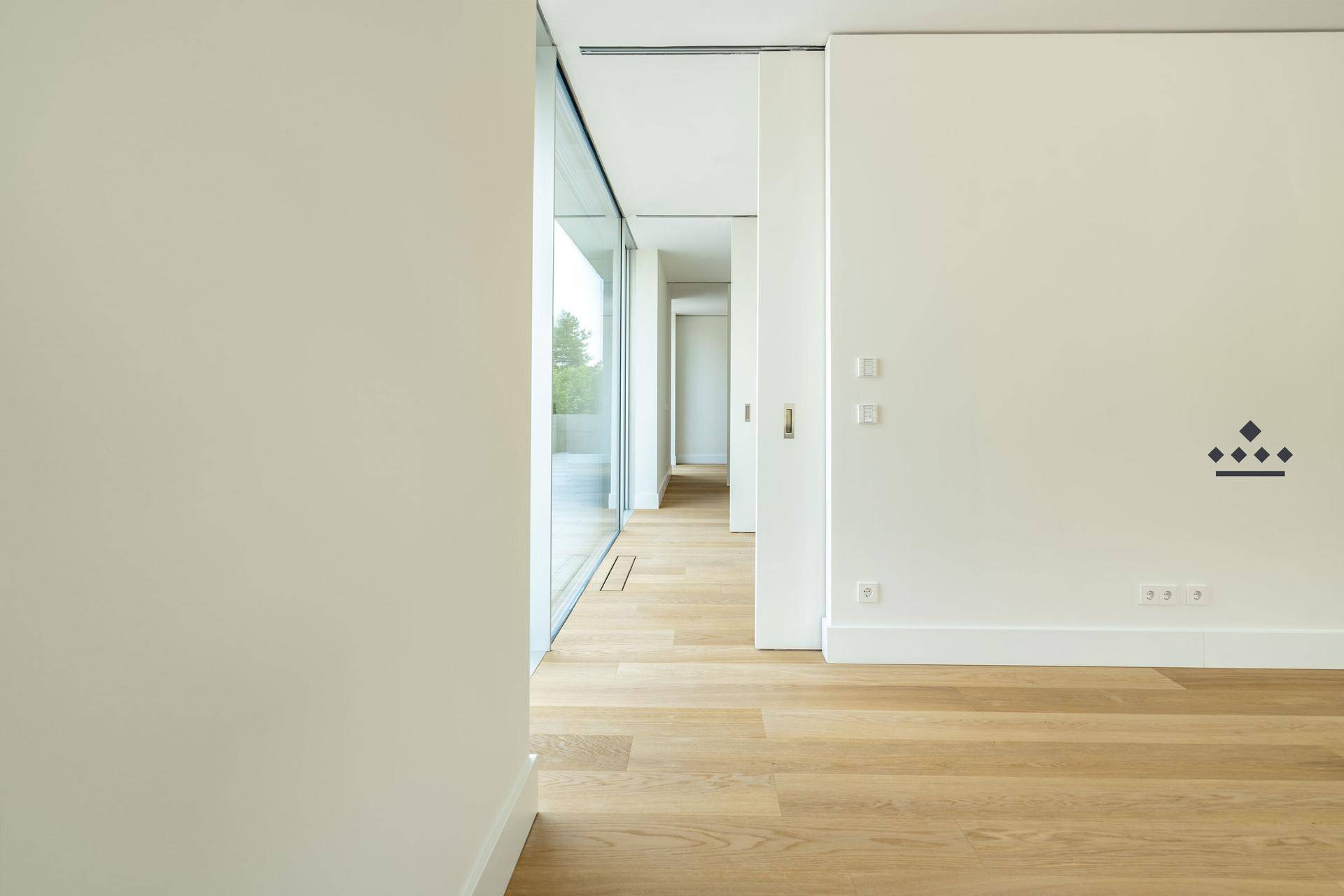 Langer, heller Flur mit Holzfußboden und großen Fenstern, die viel Tageslicht hereinlassen.