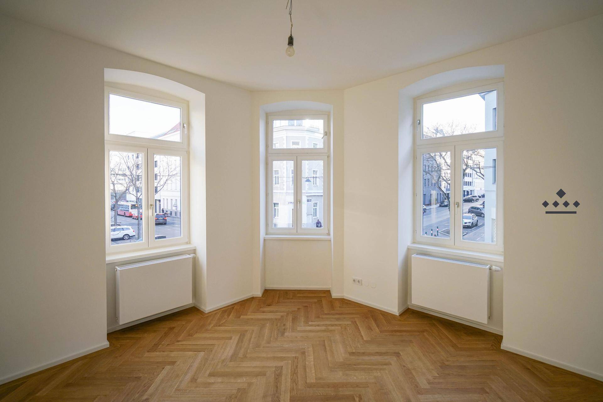 Heller Raum mit drei großen Fenstern und klassischem Fischgrätparkett.