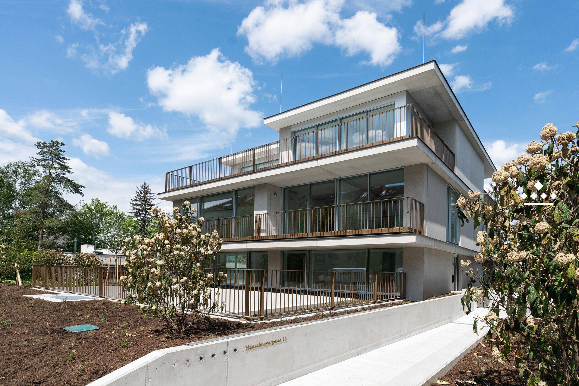Modernes Mehrfamilienhaus mit mehreren Balkonen und einer Rampe im gepflegten Gartenbereich.