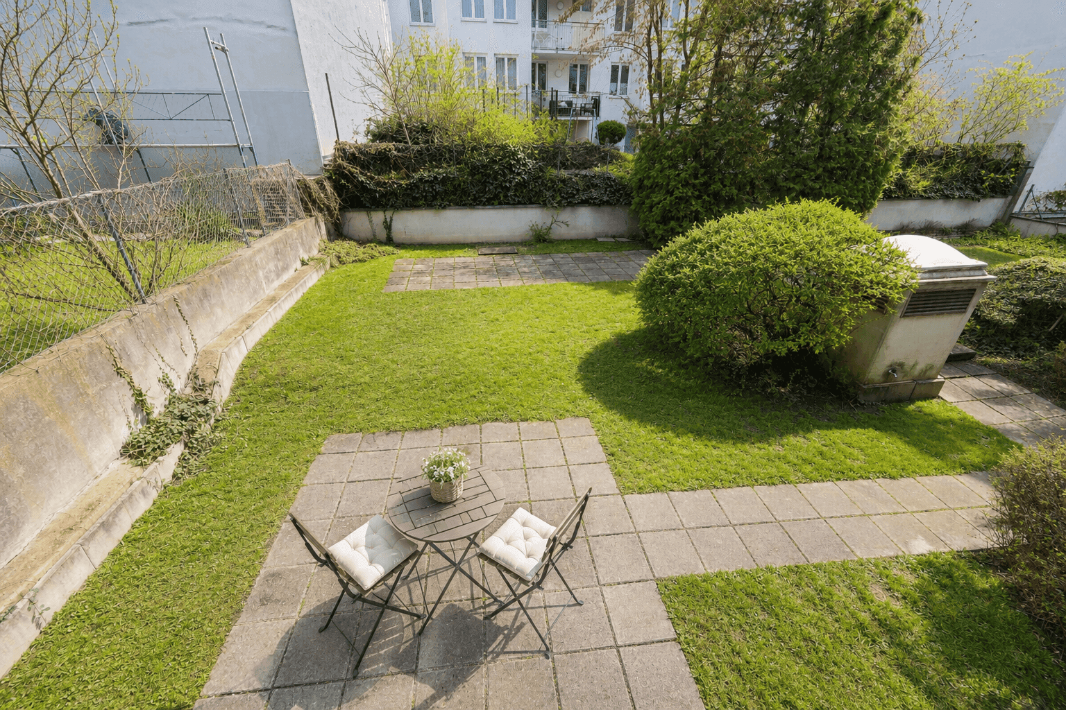 Kleiner, gepflegter Garten mit Rasenfläche, Terrasse und Sitzgelegenheit im Freien.