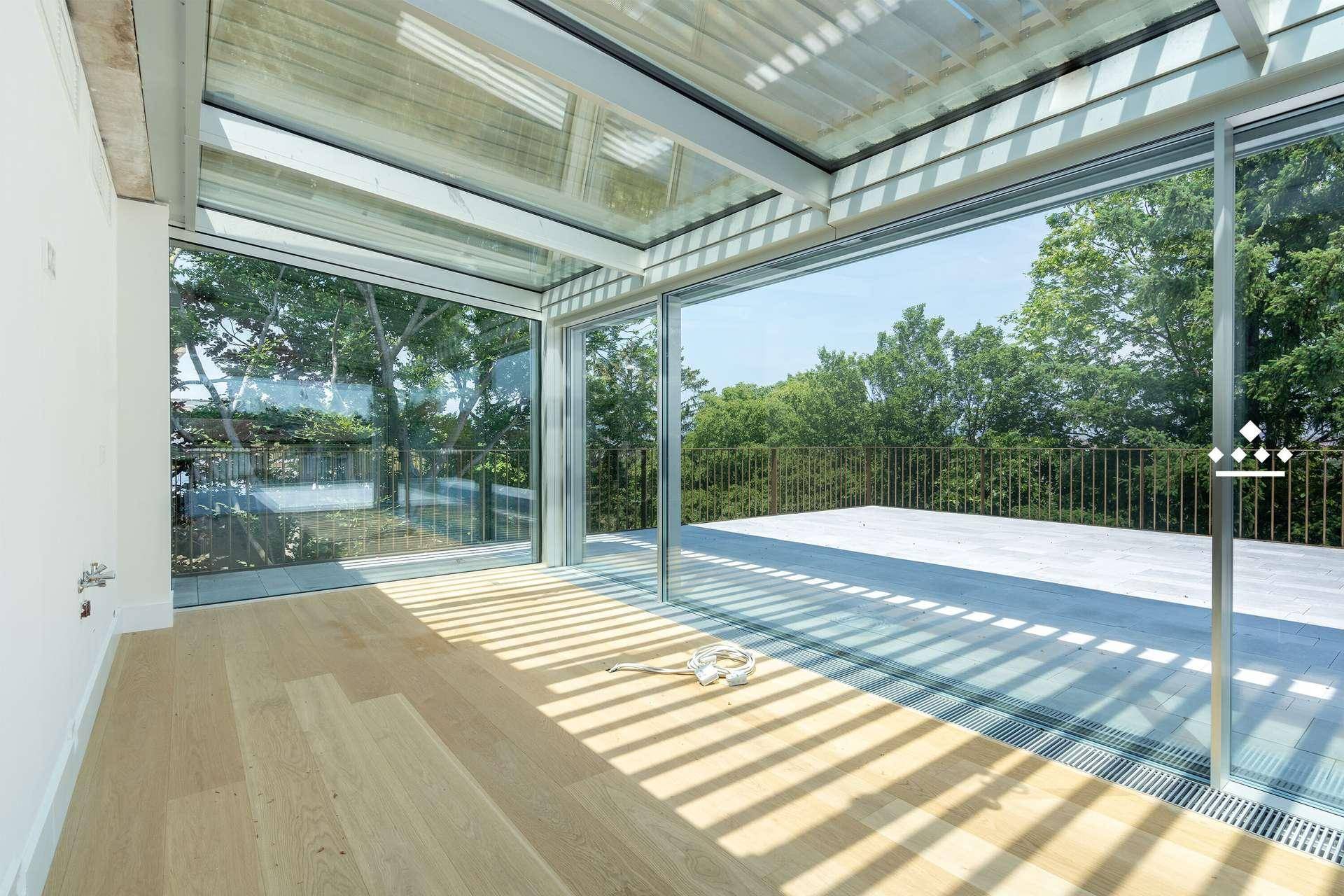 Heller Raum mit Glasdach und großen Fensterfronten, die viel Sonnenlicht hereinlassen.