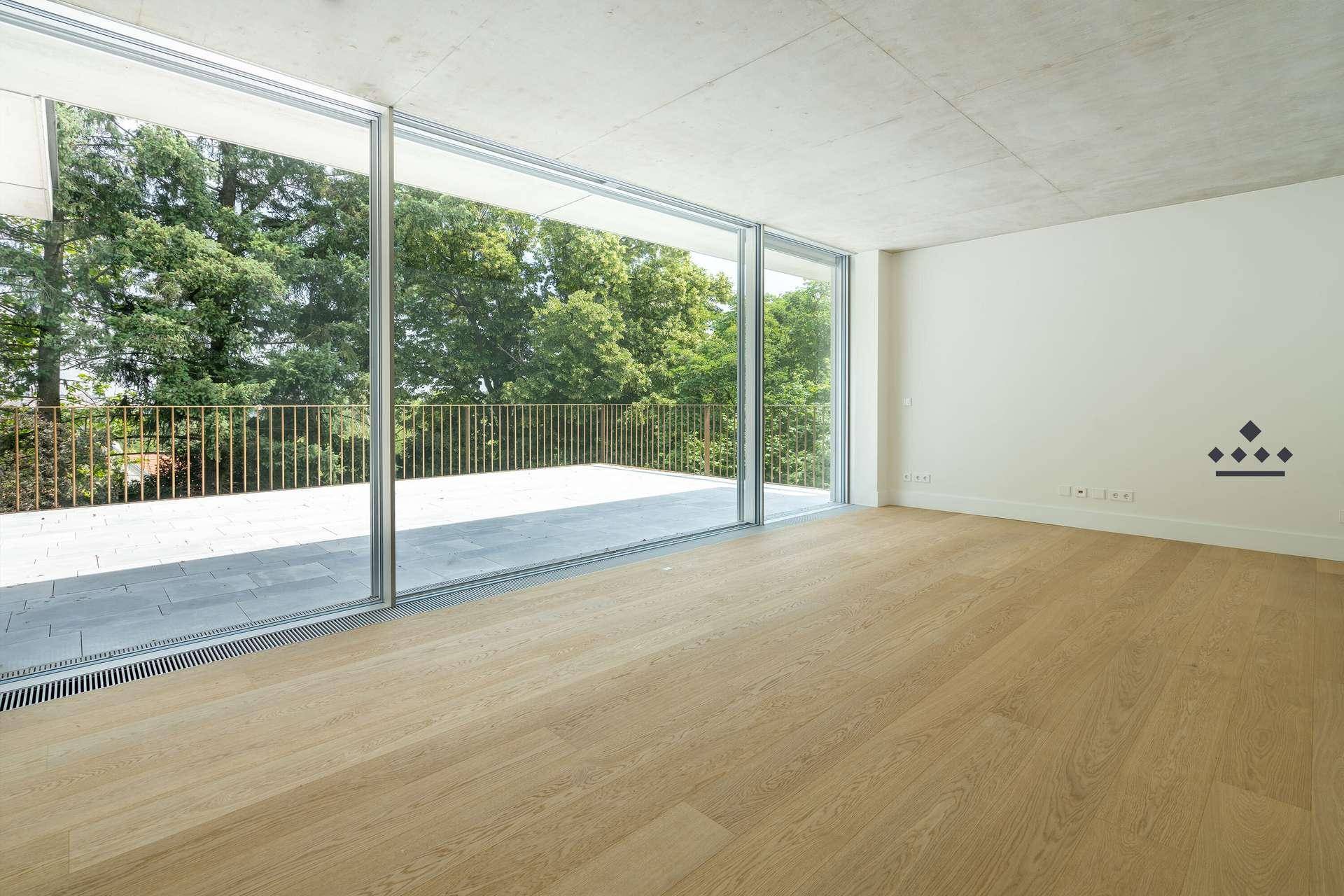Heller Raum mit Holzboden und großen Schiebetüren, die zu einer weitläufigen Terrasse führen.