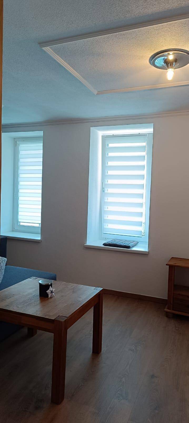 Wohnbereich mit Holztisch und zwei Fenstern, die für natürliches Licht sorgen.