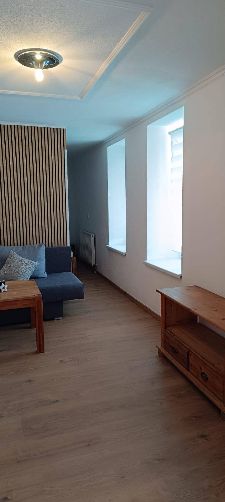 Geräumiges Wohnzimmer mit Holzboden, bequemer Couch und vertikalen Fensteröffnungen.