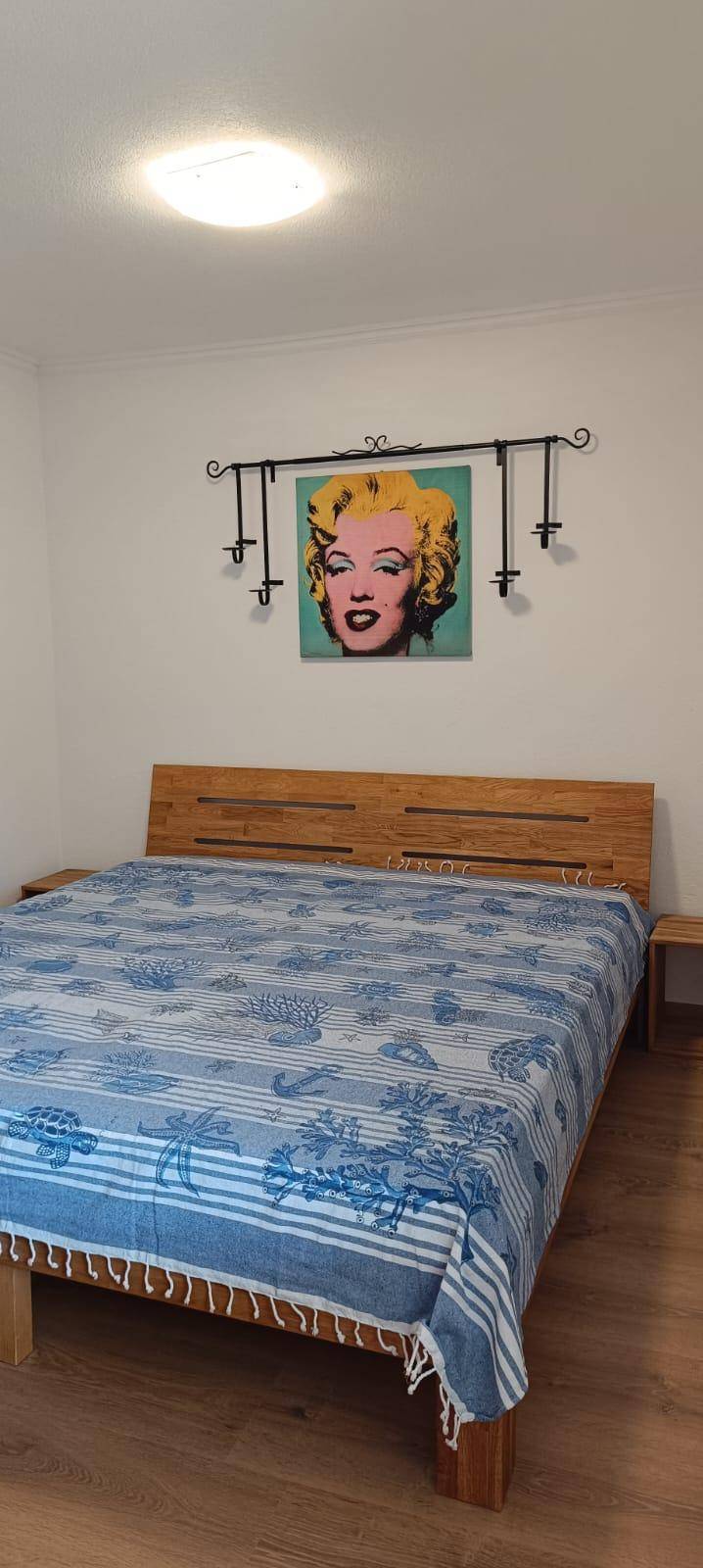 Schlafzimmer mit Holzbett, farbenfroher Bettwäsche und einem auffälligen Kunstwerk an der Wand.