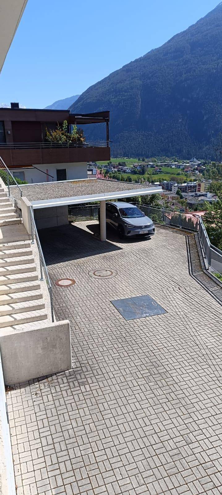 Gepflasterte Auffahrt mit Carport und einem Auto, umgeben von einer bergigen Landschaft.