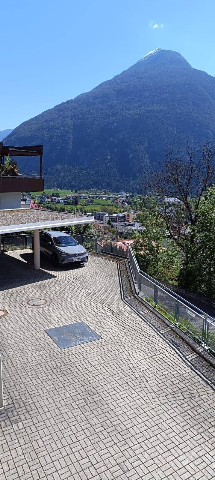 Weitläufige gepflasterte Fläche mit Carport und beeindruckendem Bergblick im Hintergrund.