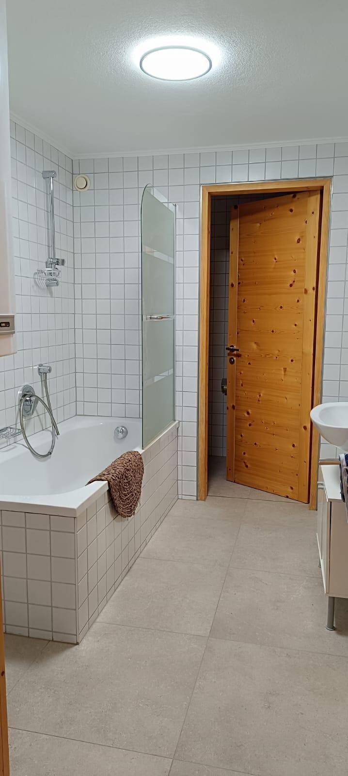 Helles Badezimmer mit Badewanne, Duschvorrichtung und weißen Wandfliesen.