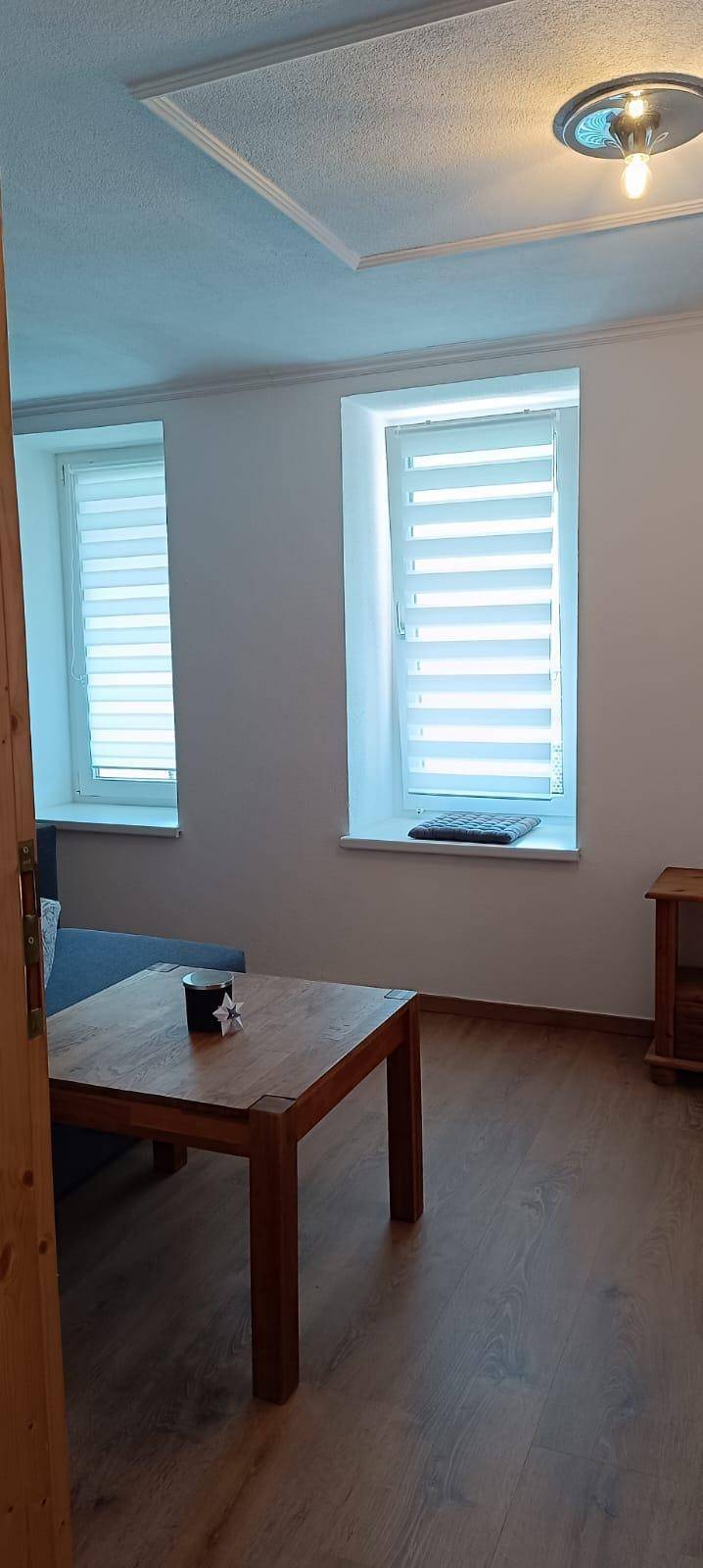 Wohnbereich mit Holztisch und zwei Fenstern, die für natürliches Licht sorgen.