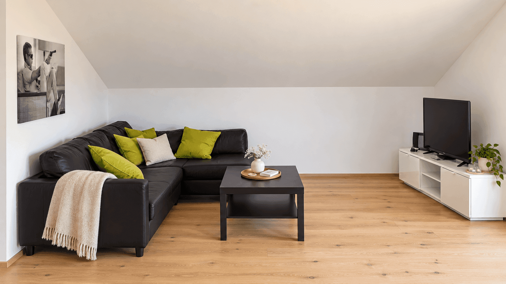 Geräumiges Wohnzimmer mit schwarzem Ecksofa, Couchtisch und Fernseher unter der Dachschräge.