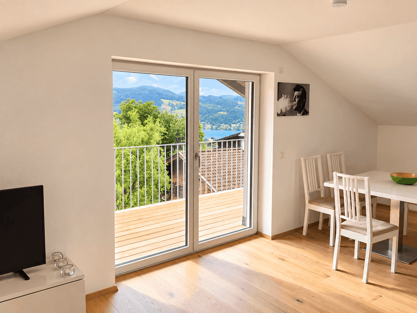 Heller Wohnbereich mit Holzboden, Schiebetür zum Balkon und malerischem Seeblick.