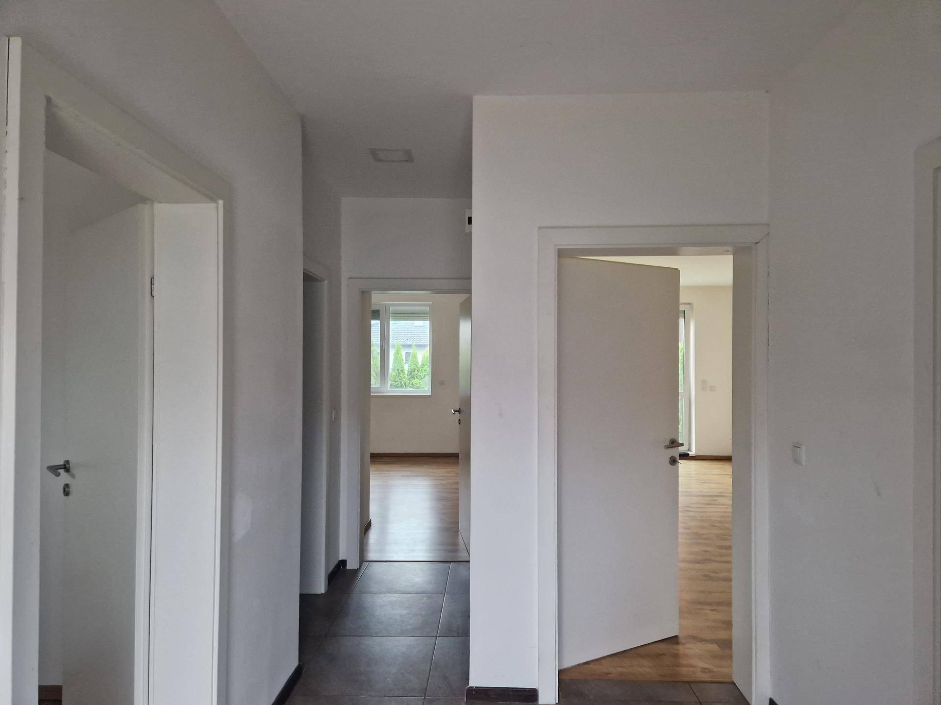 Heller Flur mit mehreren Türen, Fliesenboden im Eingangsbereich und Laminat in den Zimmern.