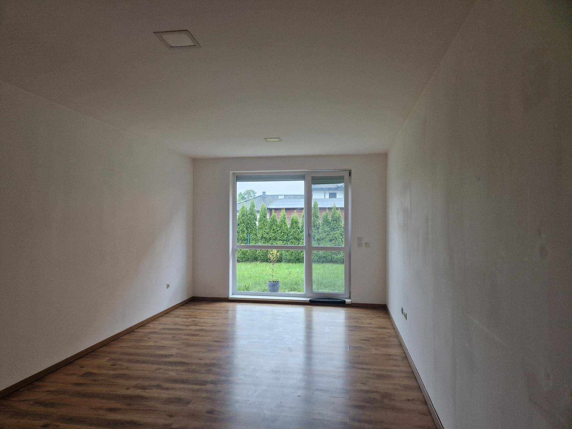 Geräumiges Zimmer mit großem Fenster und Zugang zum Garten, ausgestattet mit Laminatboden.