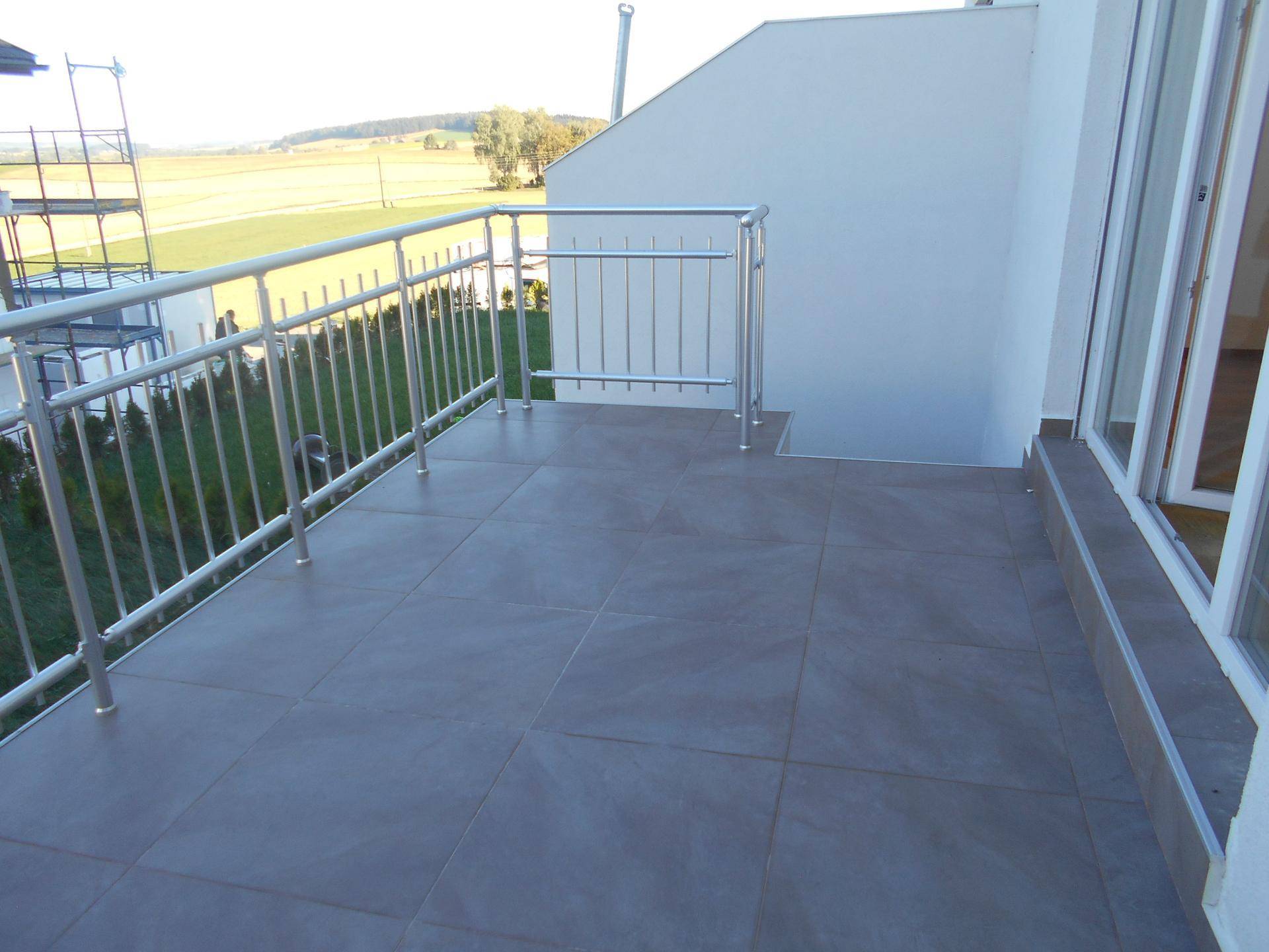 Großer Balkon mit grauen Fliesen, Metallgeländer und freiem Blick auf die umliegende Landschaft.