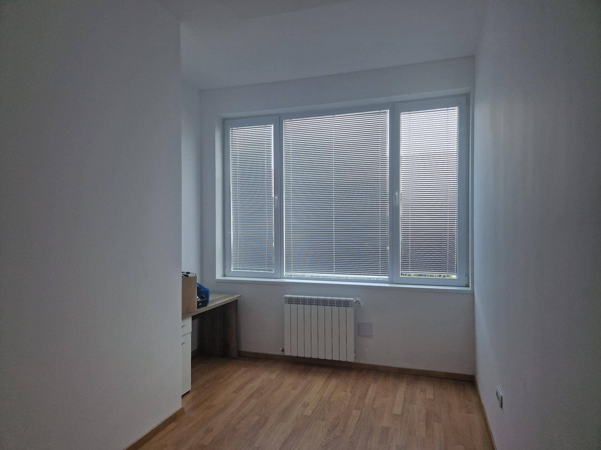 Heller, leerer Raum mit großen Fenstern, die viel Tageslicht hereinlassen, und einem Heizkörper unterhalb der Fensterbank.