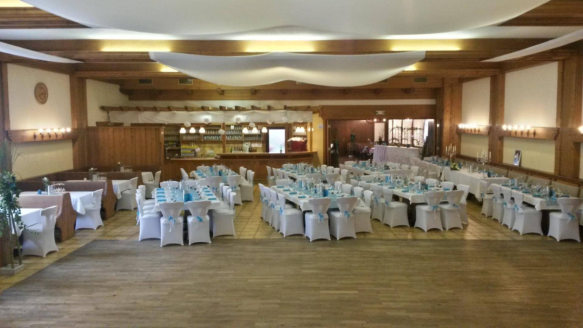 Weitläufiger Veranstaltungssaal mit festlich gedeckten Tischen und weißer Stoffdekoration an der Decke.