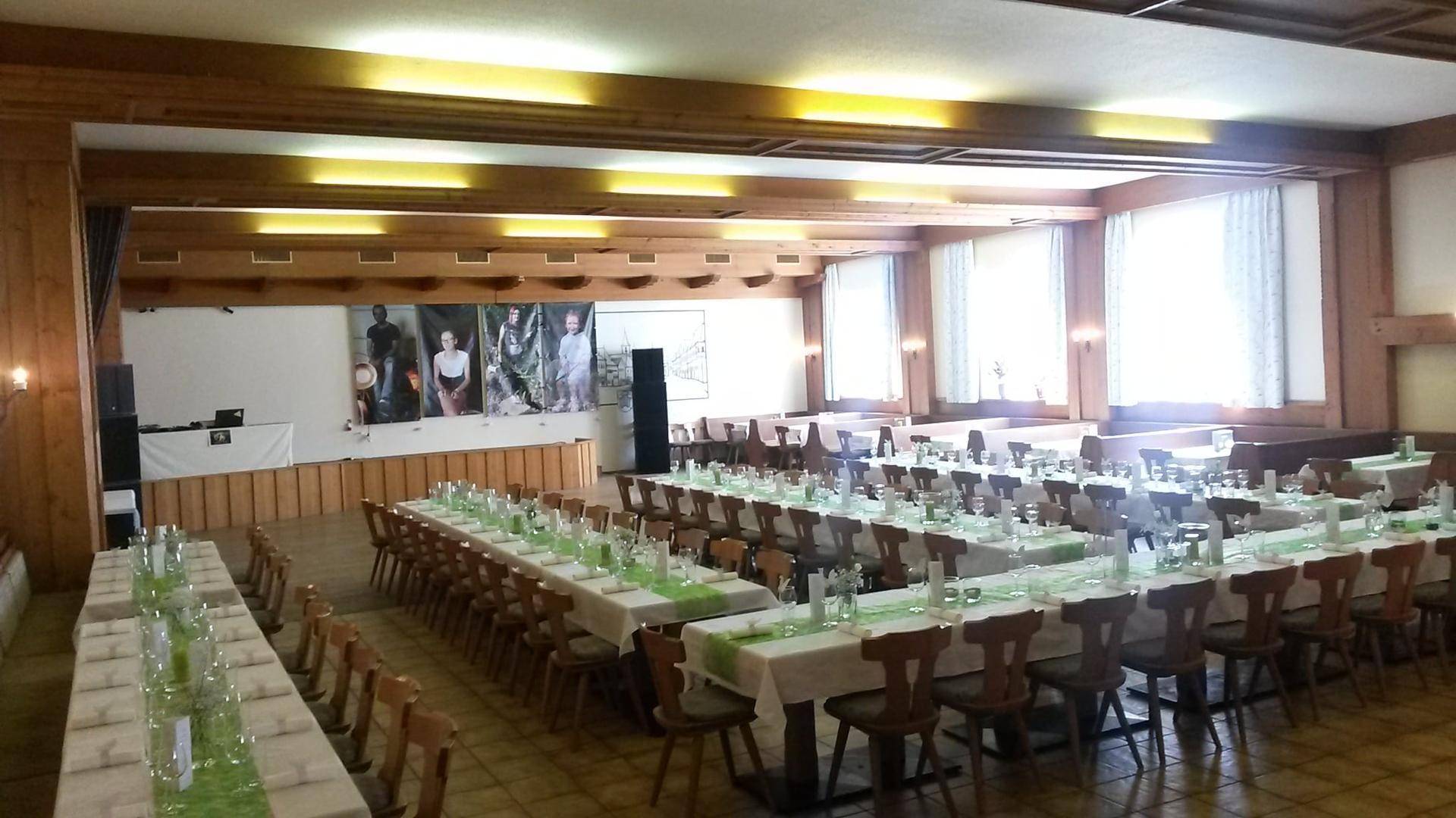 Großer Veranstaltungssaal mit vielen Tischen und Stühlen, dekoriert mit grünen Akzenten und natürlichem Licht.