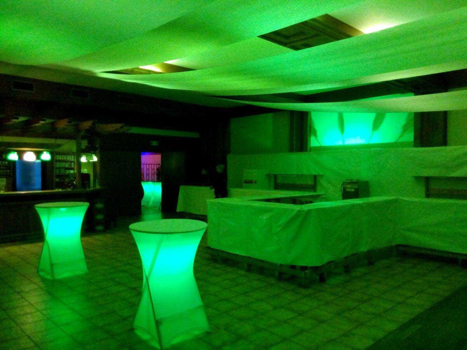 Veranstaltungsraum mit moderner grüner Beleuchtung und leuchtenden Stehtischen, bereit für eine Party.