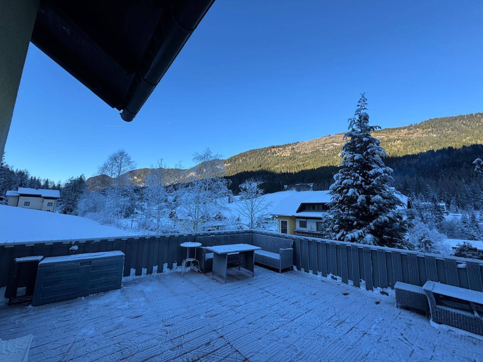 Verschneite Terrasse mit Outdoor-Möbeln und einem weiten Blick auf die winterliche Berglandschaft.