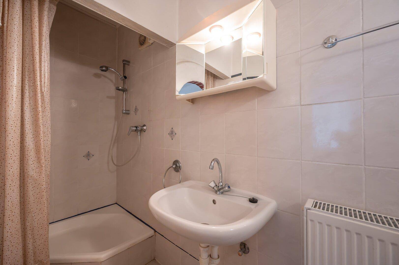 Kleines Badezimmer mit Dusche, Waschbecken und hellen Fliesen, funktional eingerichtet.