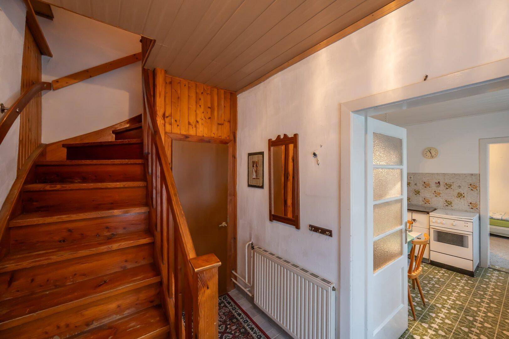 Heller Eingangsbereich mit Holztreppe und Zugang zu weiteren Räumen, inklusive einer Küche.
