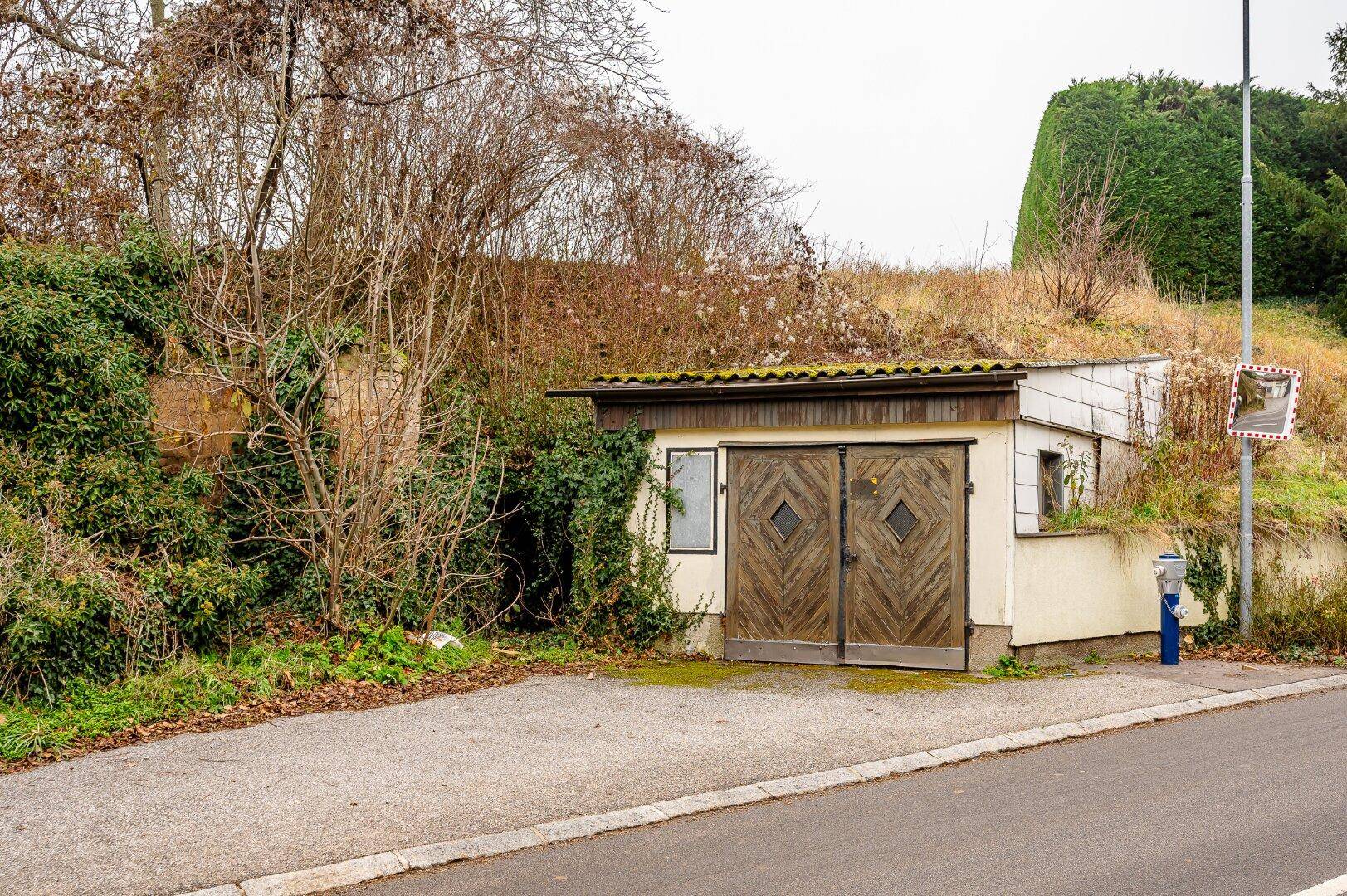Garage oder Schuppen mit Holztüren, in einen Hang gebaut, neben einer Straße.