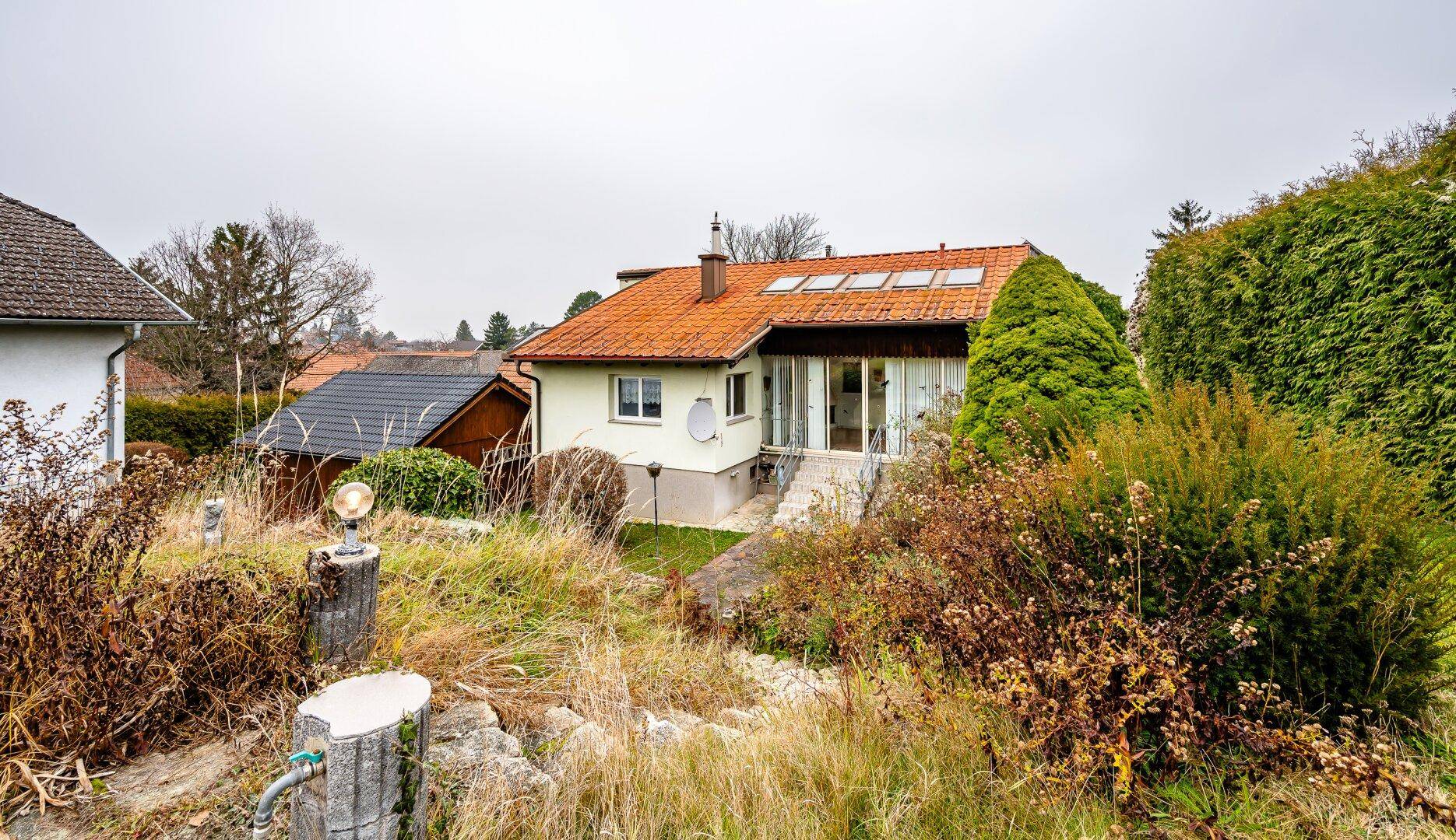 Blick auf das Haus vom Garten aus, mit Wintergarten und üppiger Vegetation im Vordergrund.