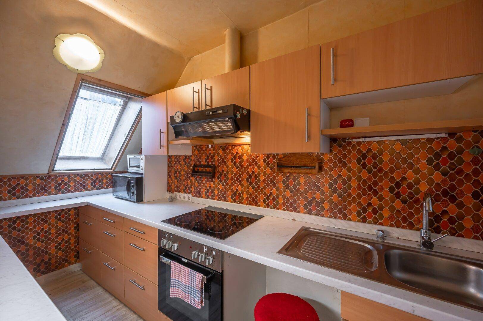 Funktionale Küche mit Kochfeld, Backofen, Mikrowelle und Spüle, unter einem Dachfenster.